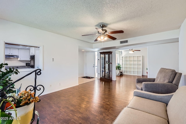 living area featuring visible vents, a ceiling fan, a textured ceiling, wood finished floors, and baseboards