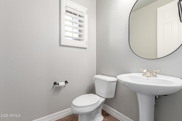 half bathroom with tile patterned floors, toilet, baseboards, and a textured wall