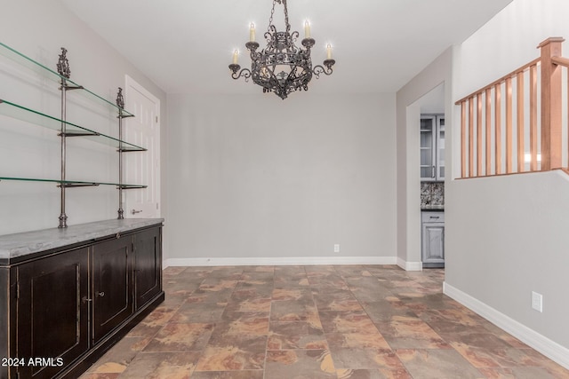 unfurnished dining area with a notable chandelier, stone finish floor, and baseboards