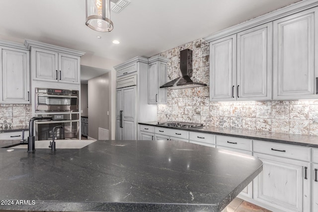 kitchen with wall chimney range hood, stainless steel appliances, backsplash, dark stone counters, and pendant lighting