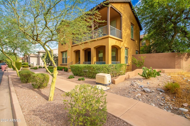 view of front facade with stucco siding, a balcony, and fence