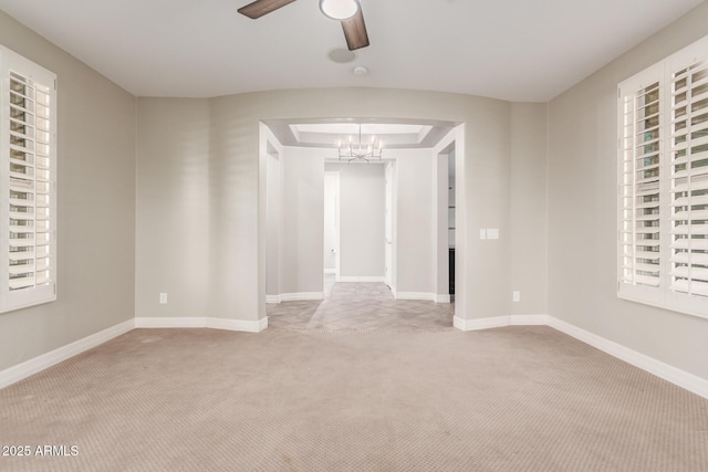 carpeted empty room featuring plenty of natural light, ceiling fan with notable chandelier, and baseboards