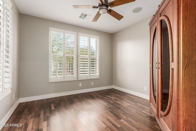 spare room featuring dark wood-style floors, visible vents, a ceiling fan, and baseboards