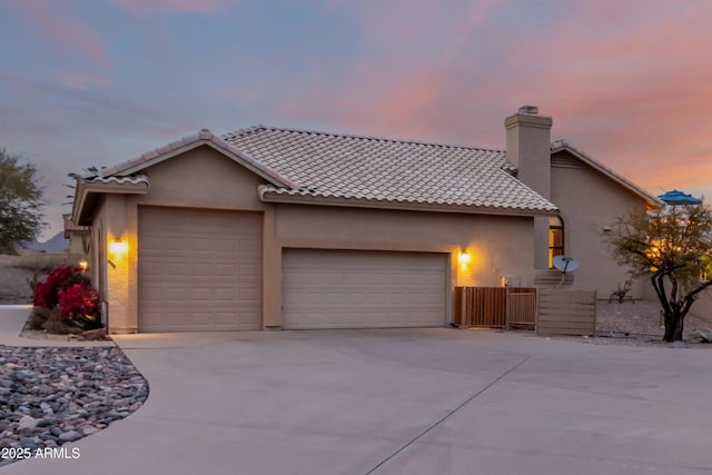 view of front of property with concrete driveway, a chimney, a tiled roof, an attached garage, and stucco siding