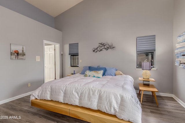 bedroom featuring wood finished floors, a towering ceiling, and baseboards