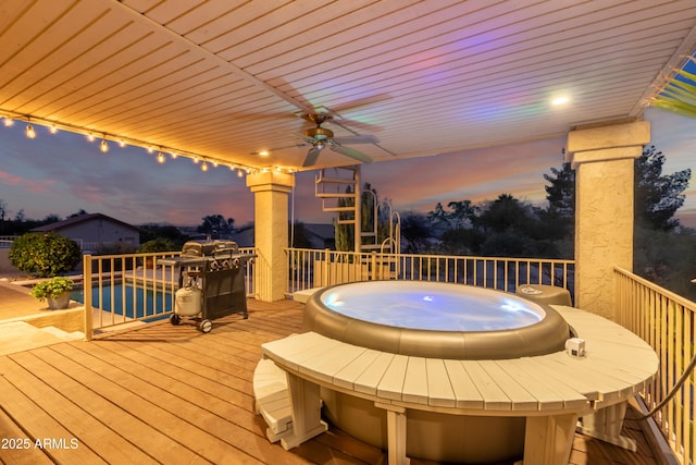 deck at dusk featuring ceiling fan and a hot tub