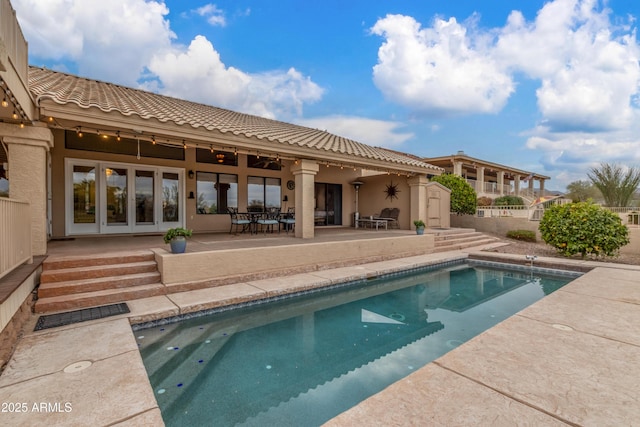 rear view of property with a patio area, a tile roof, a storage unit, and stucco siding