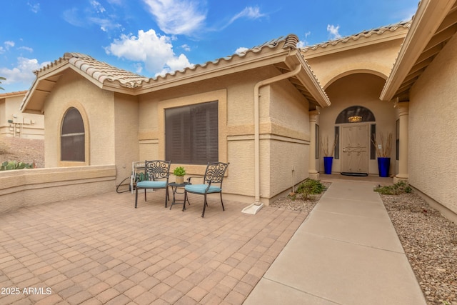 view of exterior entry featuring a tiled roof, a patio, and stucco siding