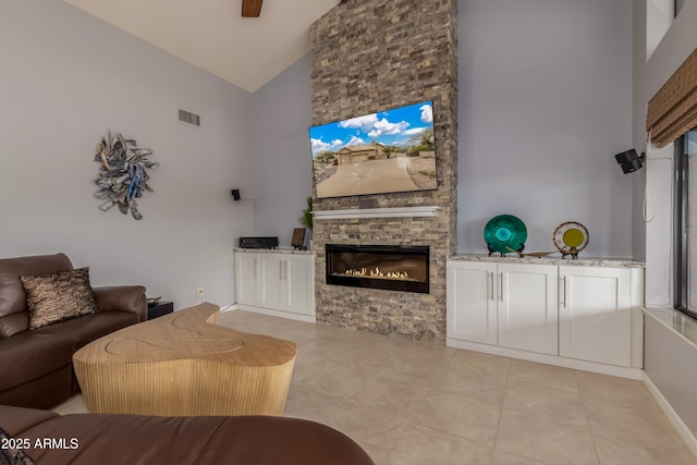 living area featuring baseboards, visible vents, a stone fireplace, high vaulted ceiling, and light tile patterned flooring