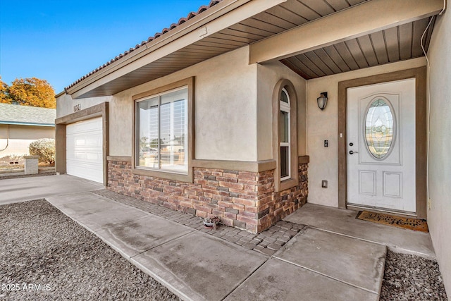 property entrance with a garage, a tile roof, stone siding, driveway, and stucco siding