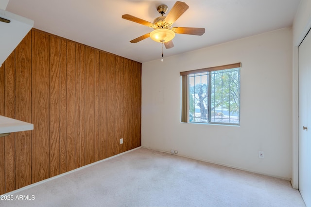 spare room featuring wooden walls, carpet floors, and ceiling fan