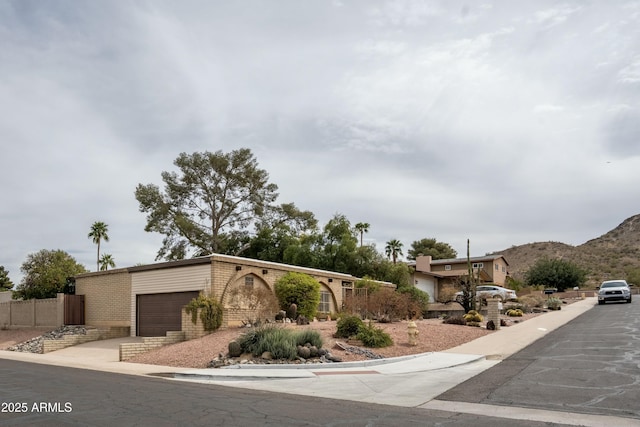 view of front facade with fence, a mountain view, concrete driveway, a garage, and brick siding