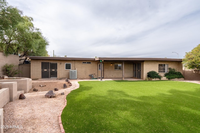 rear view of property with brick siding, fence, central AC unit, a lawn, and a patio