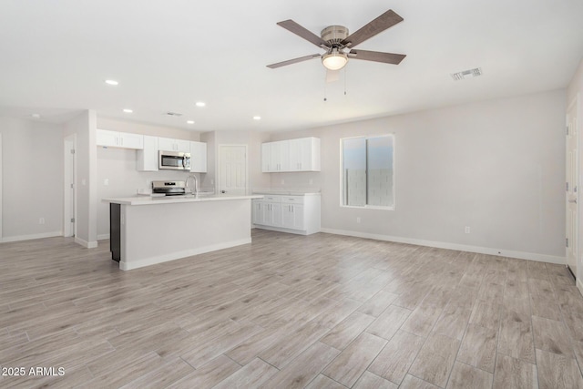 kitchen featuring stainless steel appliances, visible vents, white cabinetry, open floor plan, and light wood finished floors