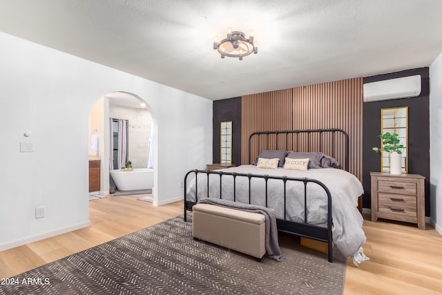 bedroom featuring a wall unit AC, ensuite bathroom, a textured ceiling, and hardwood / wood-style flooring