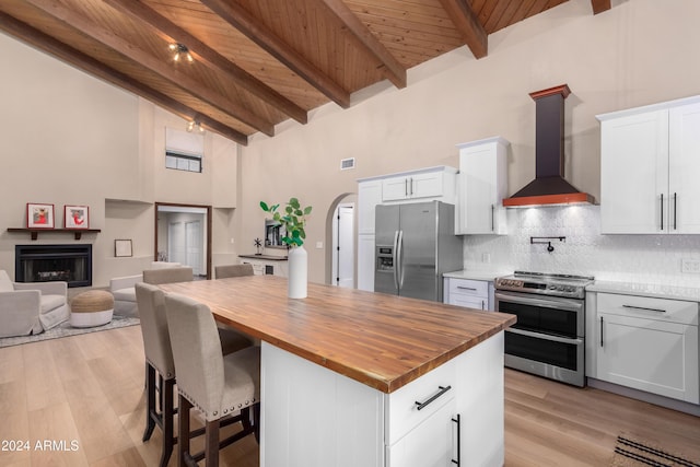 kitchen with white cabinetry, stainless steel appliances, wall chimney range hood, and light hardwood / wood-style floors