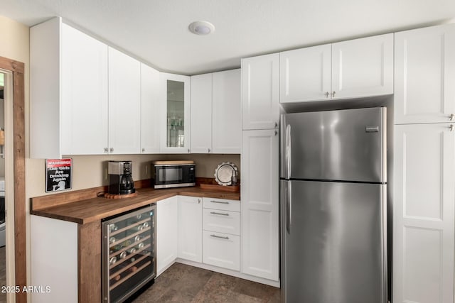 kitchen featuring wine cooler, butcher block counters, white cabinetry, freestanding refrigerator, and glass insert cabinets