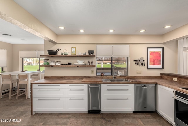 kitchen featuring visible vents, butcher block countertops, stainless steel appliances, white cabinetry, and a sink