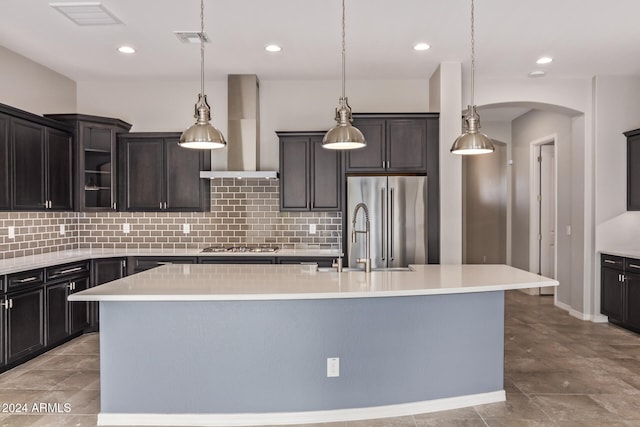 kitchen featuring pendant lighting, an island with sink, stainless steel appliances, and wall chimney range hood