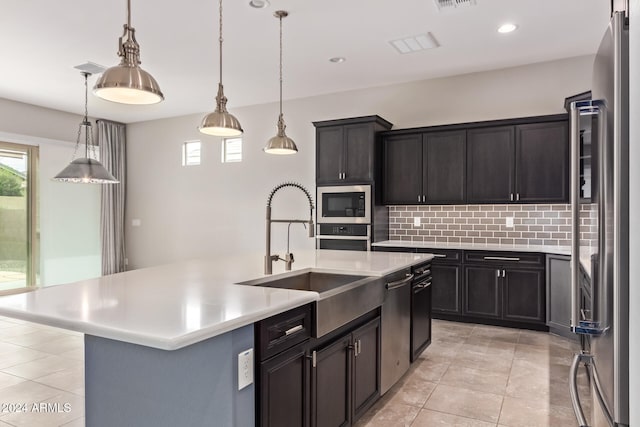 kitchen featuring sink, stainless steel appliances, decorative light fixtures, decorative backsplash, and a center island with sink