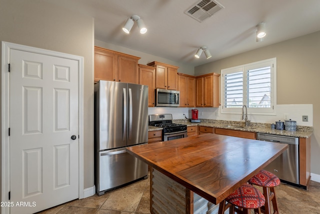 kitchen featuring appliances with stainless steel finishes, a sink, baseboards, light stone countertops, and brown cabinets