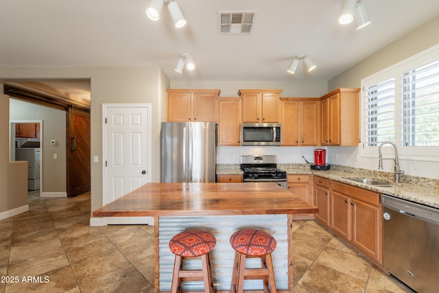 kitchen featuring stainless steel appliances, a sink, washer / dryer, a barn door, and light stone counters