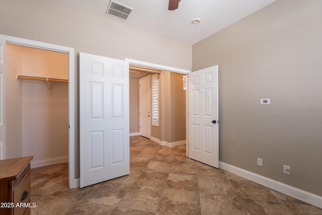 unfurnished bedroom with baseboards, a closet, a walk in closet, and stone finish flooring