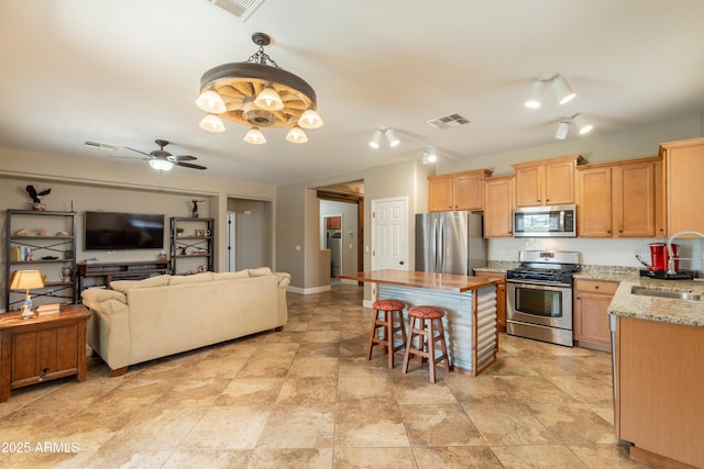 kitchen with stainless steel appliances, a kitchen breakfast bar, light stone countertops, open floor plan, and a sink