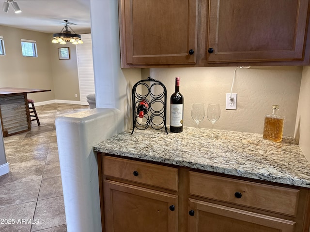 kitchen with baseboards, light stone counters, light tile patterned flooring, and a chandelier
