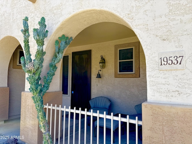 entrance to property featuring stucco siding and fence