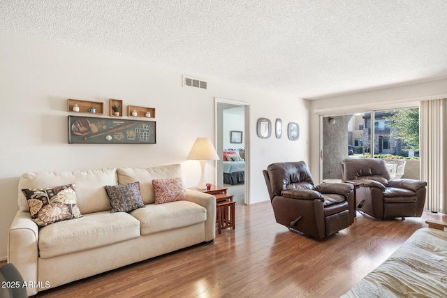 living area with visible vents, a textured ceiling, and wood finished floors