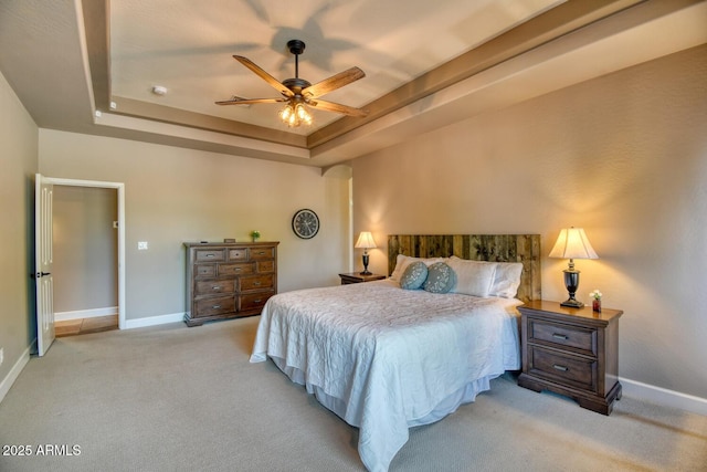 bedroom featuring baseboards, ceiling fan, a tray ceiling, and light colored carpet