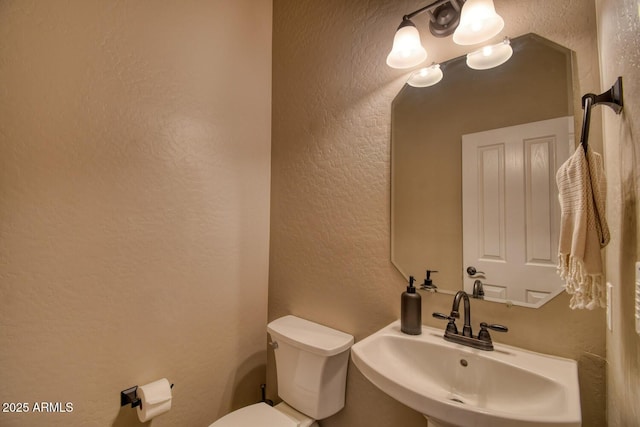 bathroom featuring toilet, a textured wall, and a sink