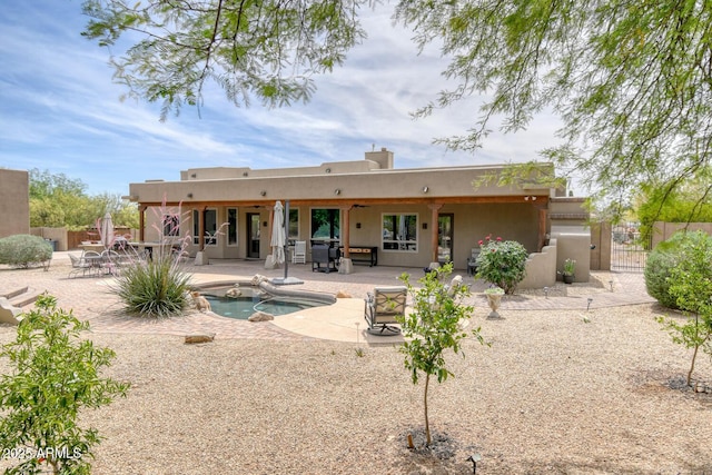 back of property featuring fence, a jacuzzi, stucco siding, a gate, and a patio area