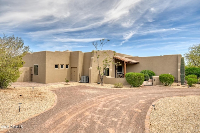adobe home featuring central AC unit, a gate, fence, curved driveway, and stucco siding