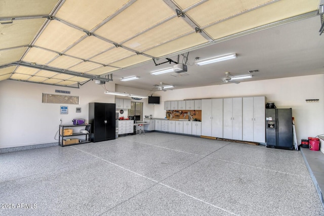 garage featuring baseboards, a garage door opener, and black refrigerator with ice dispenser