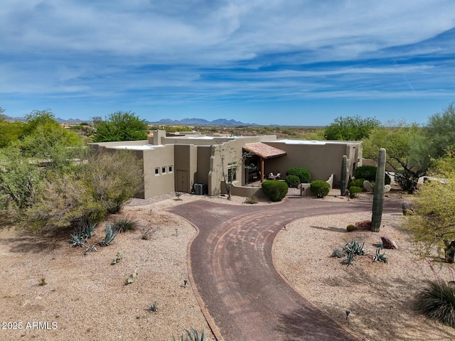 pueblo-style house with a mountain view, stucco siding, and central AC unit