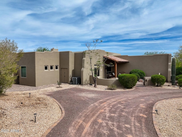 pueblo revival-style home with curved driveway, a gate, stucco siding, and cooling unit