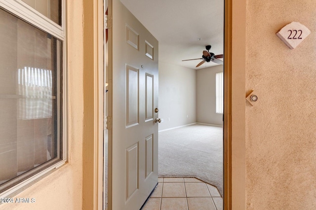 corridor featuring light tile patterned floors, baseboards, and light colored carpet