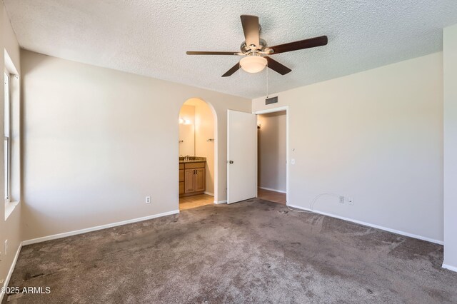 unfurnished bedroom featuring arched walkways, light colored carpet, baseboards, visible vents, and a textured ceiling