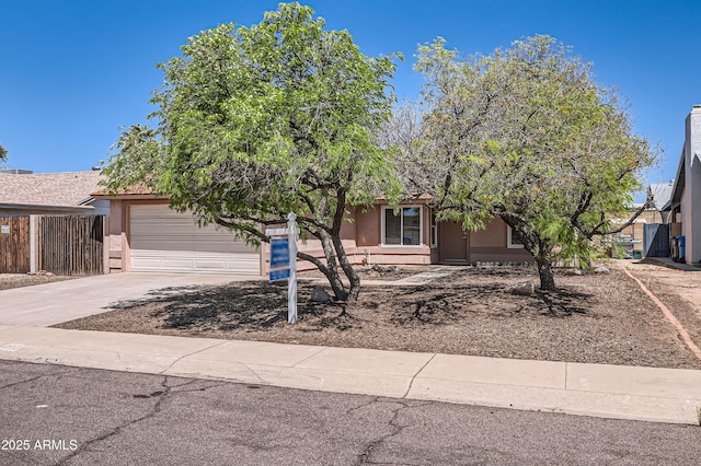 view of property hidden behind natural elements with driveway, fence, stucco siding, and a garage