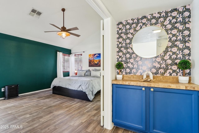 bedroom with wallpapered walls, an accent wall, wood finished floors, vaulted ceiling, and ceiling fan
