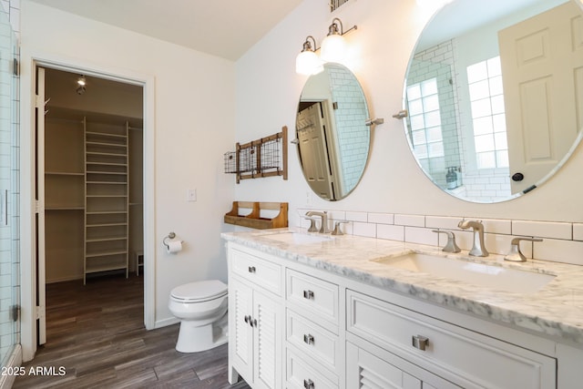 bathroom with wood finished floors, toilet, double vanity, a shower with shower door, and a walk in closet