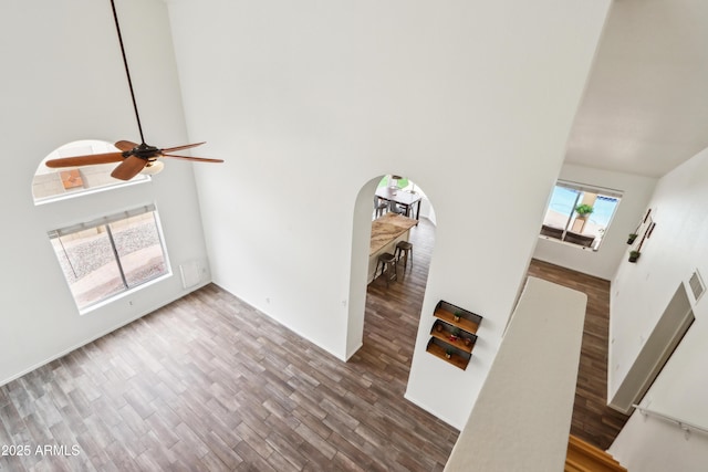 unfurnished living room featuring a towering ceiling, ceiling fan, wood finished floors, and arched walkways