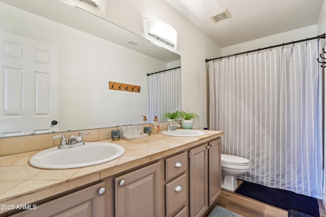 bathroom with toilet, double vanity, and wood finished floors