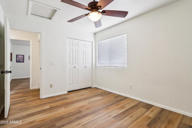 unfurnished bedroom with attic access, light wood-style floors, baseboards, and a closet