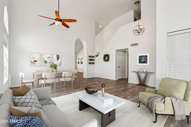 living area with arched walkways, high vaulted ceiling, a ceiling fan, wood finished floors, and a chandelier