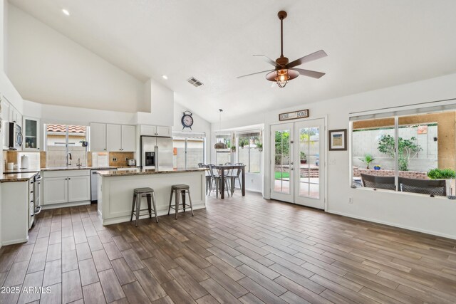 kitchen featuring appliances with stainless steel finishes, a ceiling fan, a kitchen island, high vaulted ceiling, and white cabinets