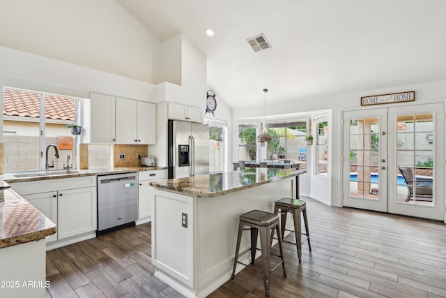 kitchen featuring stainless steel appliances, a sink, light stone counters, wood finished floors, and high vaulted ceiling