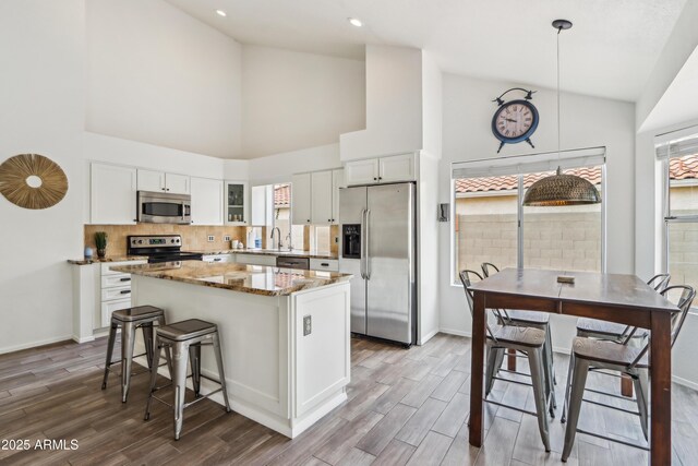 kitchen with stainless steel appliances, high vaulted ceiling, a center island, wood finished floors, and a sink
